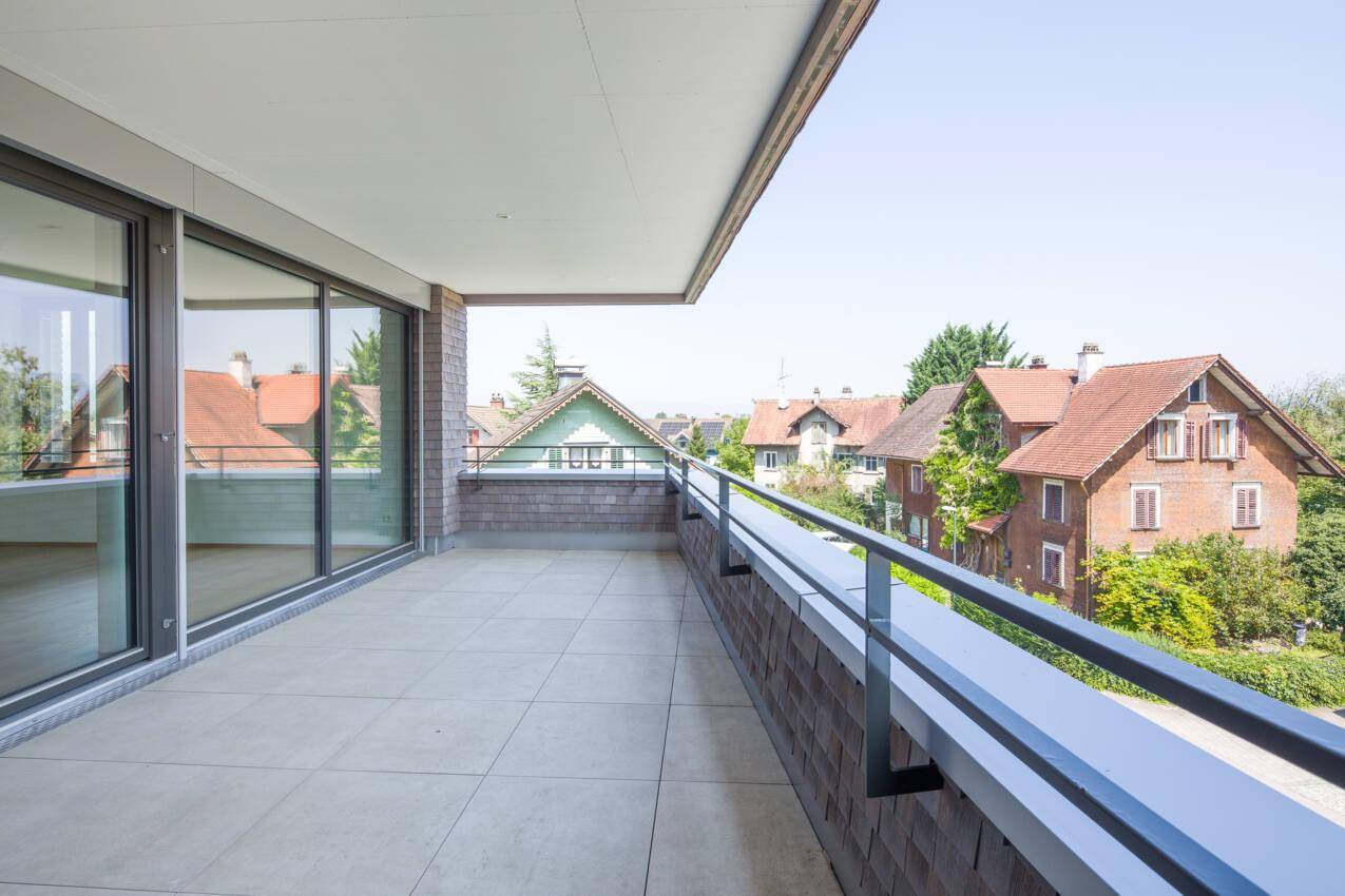 Großer Balkon mit Fliesenboden und Blick auf die umliegenden Häuser und Berge.