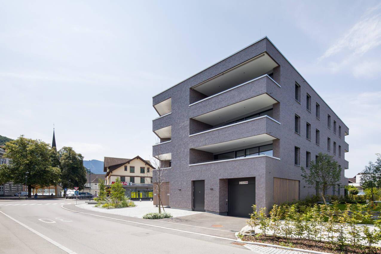 Ansicht des modernen Mehrfamilienhauses mit Balkonen und umliegender Infrastruktur unter blauem Himmel.