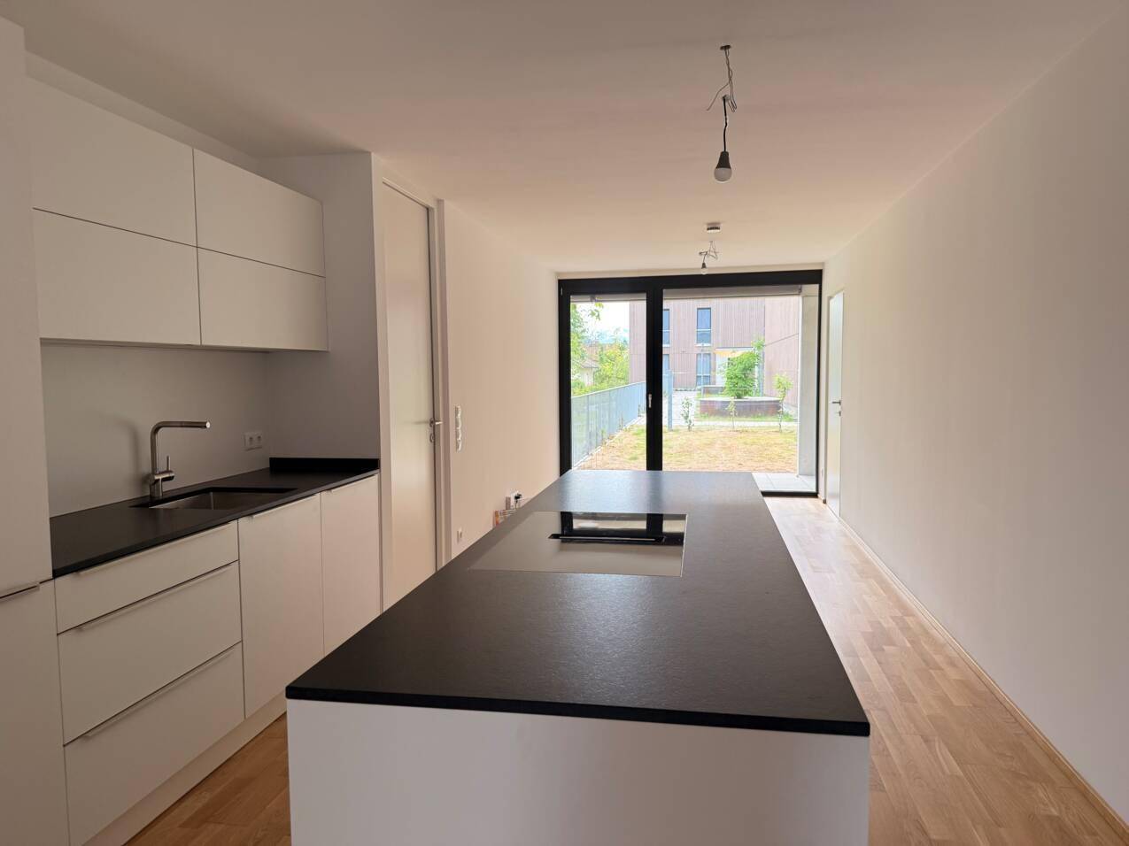 Moderne offene Küche mit weißer Kücheninsel, dunkler Arbeitsplatte und Zugang zum Außenbereich.