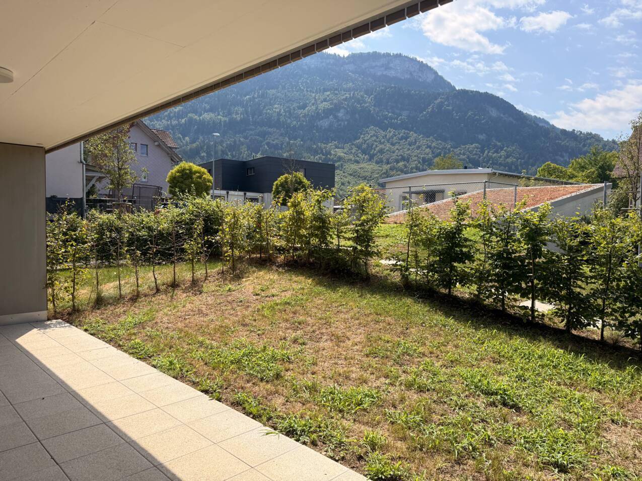 Außenbereich mit gepflasterter Terrasse, Rasenfläche, Hecken und beeindruckendem Bergblick.