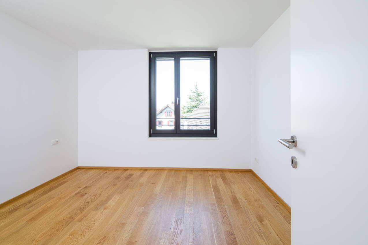 Helles Schlafzimmer mit Eichenparkettboden und einem großen Fenster mit Blick ins Grüne.