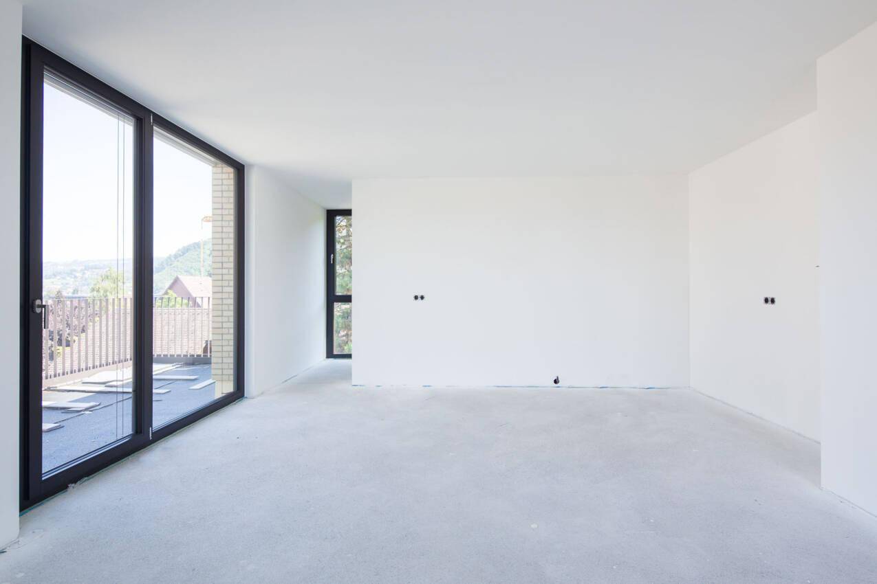 Heller, unfertiger Wohnraum mit großen Fenstern und Zugang zu einem zukünftigen Außenbereich.