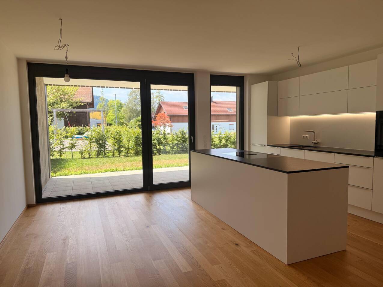 Offene, moderne Küche mit weißer Kochinsel, Holzboden und großem Fenster zum Garten.
