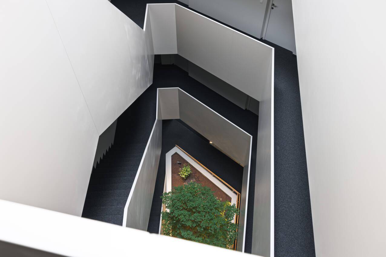 Modernes Treppenhaus mit geometrischen Linien und einem begrünten Innenhof im Zentrum.