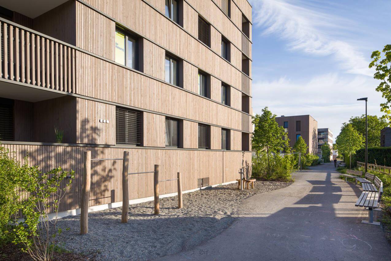 Moderne Holzfassade eines Mehrfamilienhauses mit Balkonen und einem Spielbereich im Freien.
