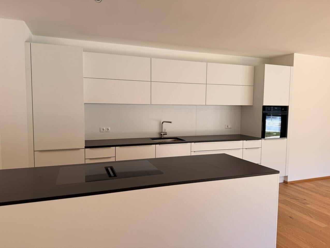Moderne, helle Küche mit weißen Schränken, dunkler Arbeitsplatte und integrierten Geräten.