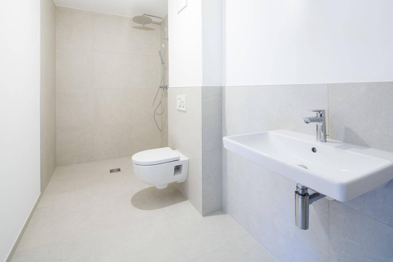 Modernes Badezimmer mit ebenerdiger Dusche, wandhängendem WC und hellem Fliesenboden.