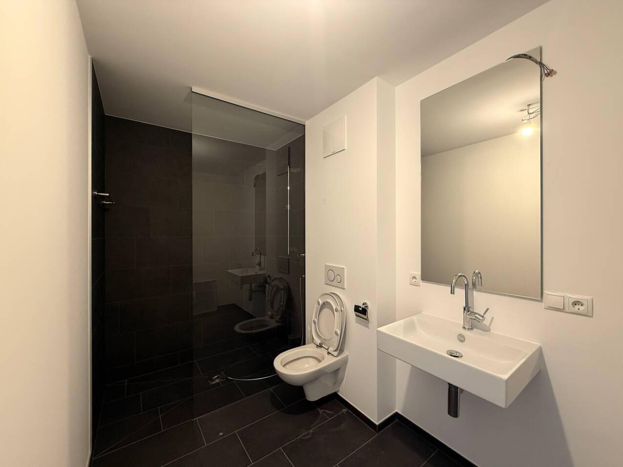 Modernes Badezimmer mit dunklen Fliesen, bodengleicher Dusche und wandhängendem WC.
