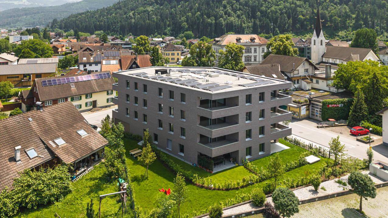 Luftaufnahme des modernen Wohngebäudes mit Solaranlage auf dem Flachdach und grüner Umgebung.