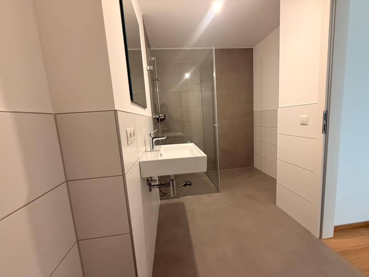 Modernes Badezimmer mit Einzelwaschbecken, Spiegel und einer begehbaren Dusche mit Glasabtrennung.