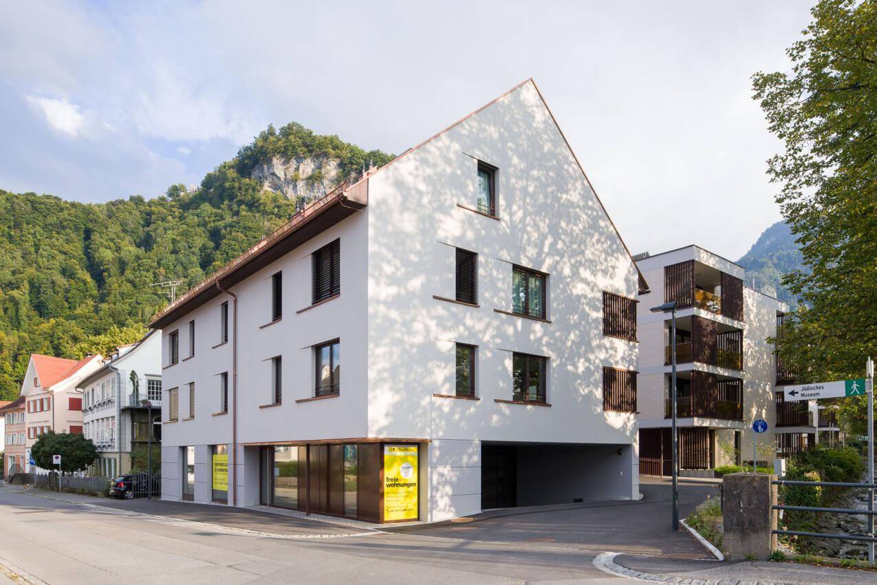 Mehrfamilienhaus mit moderner Architektur an einer Straße, umgeben von Bergen.