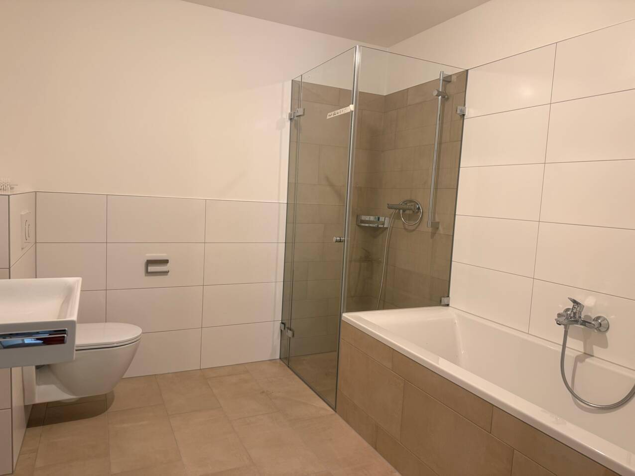 Modernes Badezimmer mit Dusche, Badewanne, wandhängendem WC und Waschbecken, hell gefliest.