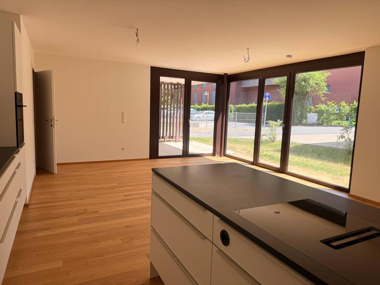 Offener Wohnbereich mit Holzboden, großen Fenstern und direktem Zugang zur Terrasse.