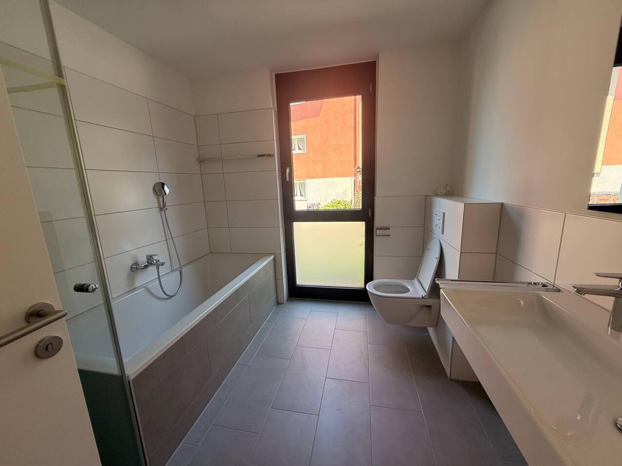 Helles Badezimmer mit Badewanne, WC, Einzelwaschbecken und Fenster für Tageslicht.