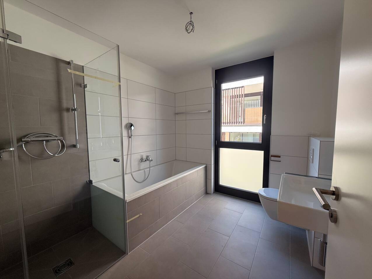 Modernes Badezimmer mit Badewanne, ebenerdiger Dusche, wandhängendem WC und Fenster.