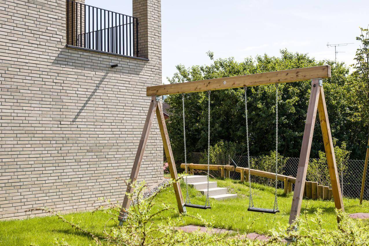 Kinderspielplatz mit Schaukeln in einer grünen Gartenanlage neben dem Gebäude.