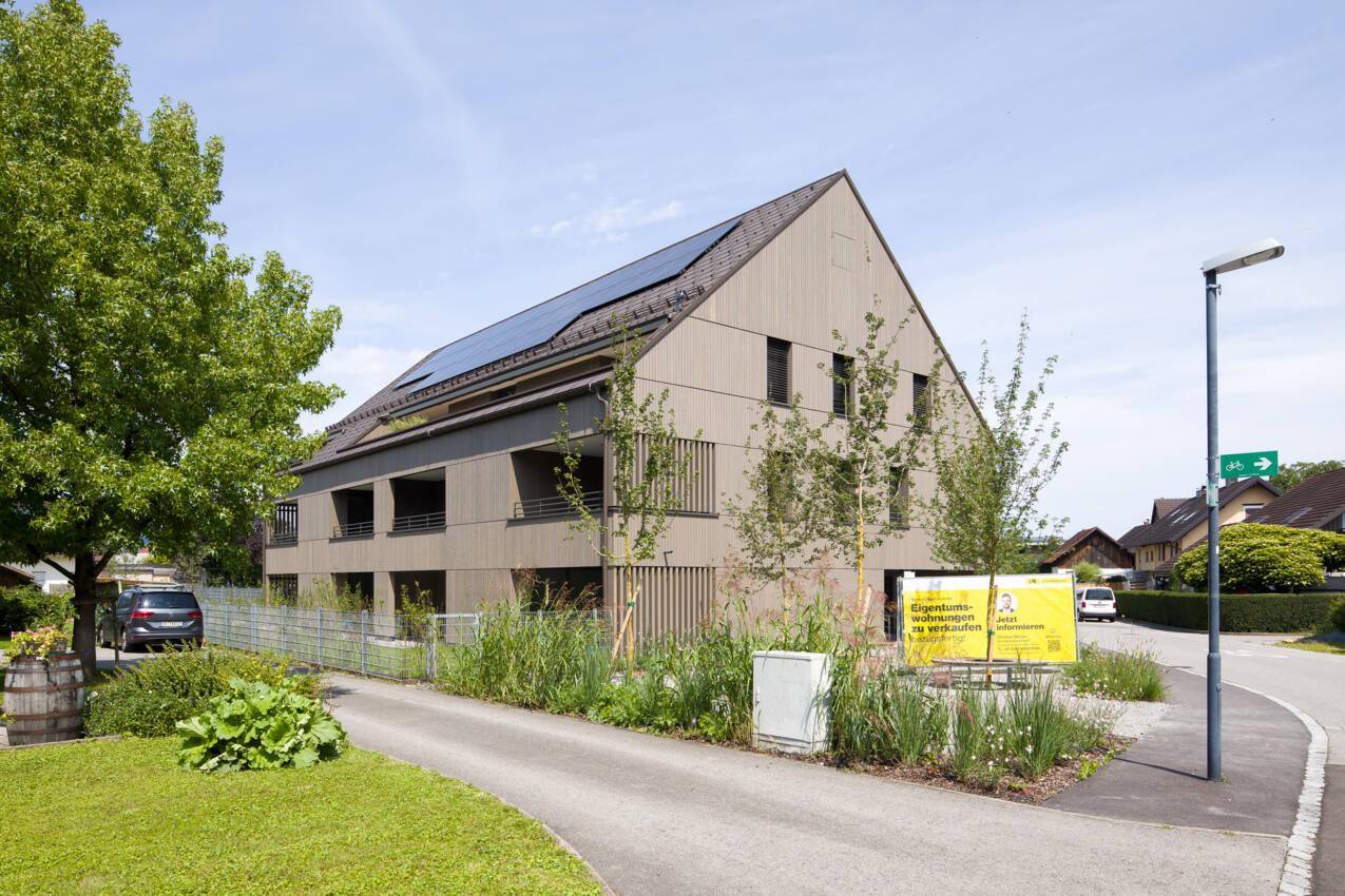 Modernes Mehrfamilienhaus mit Photovoltaikanlage auf dem Satteldach und grüner Umgebung.