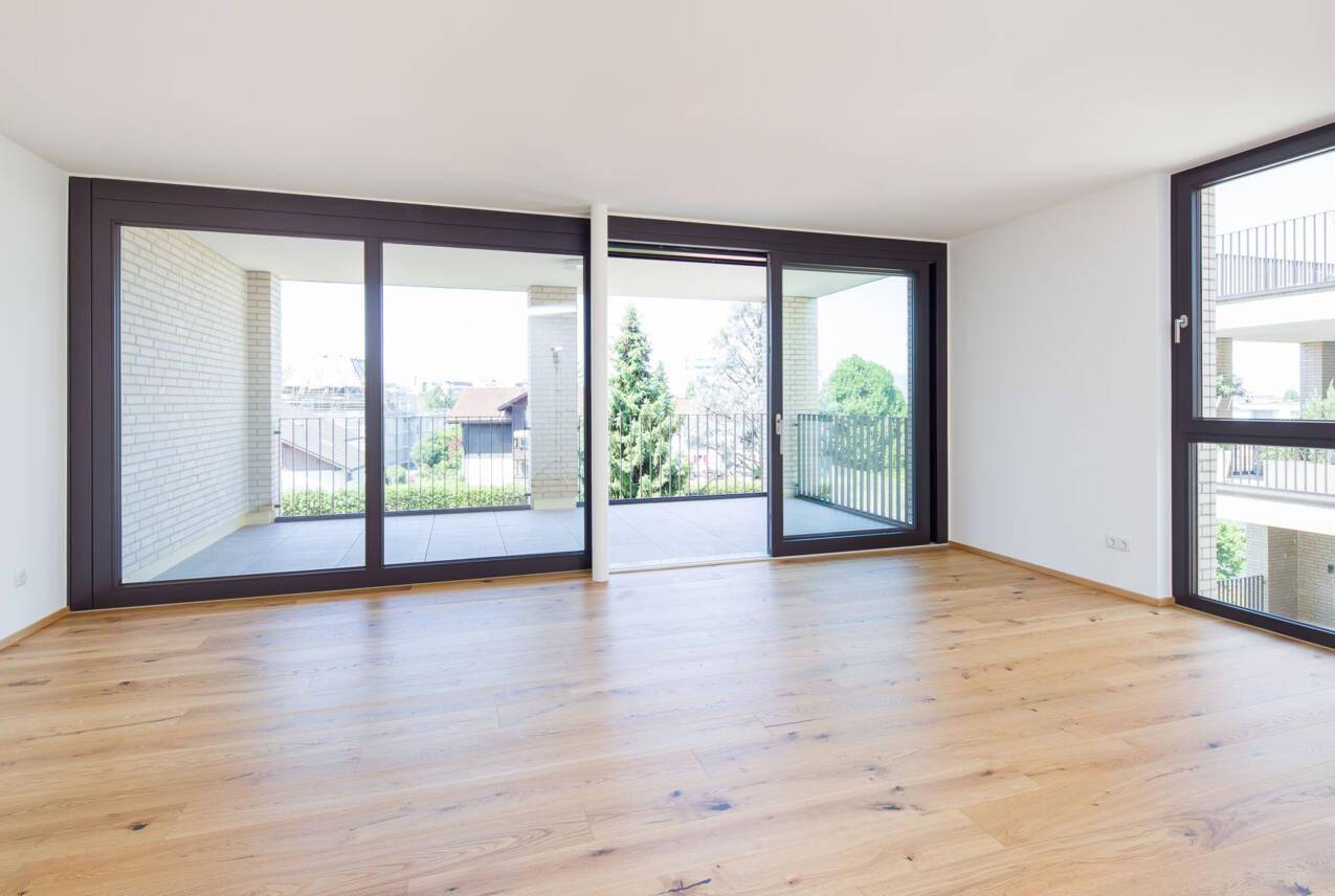 Heller Wohnbereich mit Echtholzboden und breiten Schiebetüren, die auf einen Balkon führen.