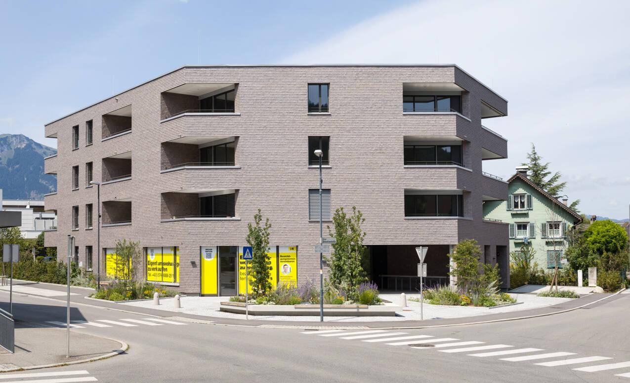 Eckansicht eines modernen Wohnhauses mit Holzschindelfassade und großen Fenstern an einer Kreuzung.