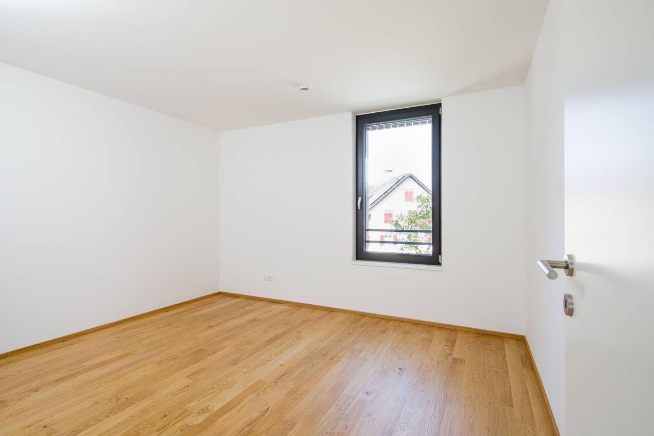 Helles Schlafzimmer mit Holzboden und einem Fenster, bietet eine neutrale Basis für individuelle Gestaltung.