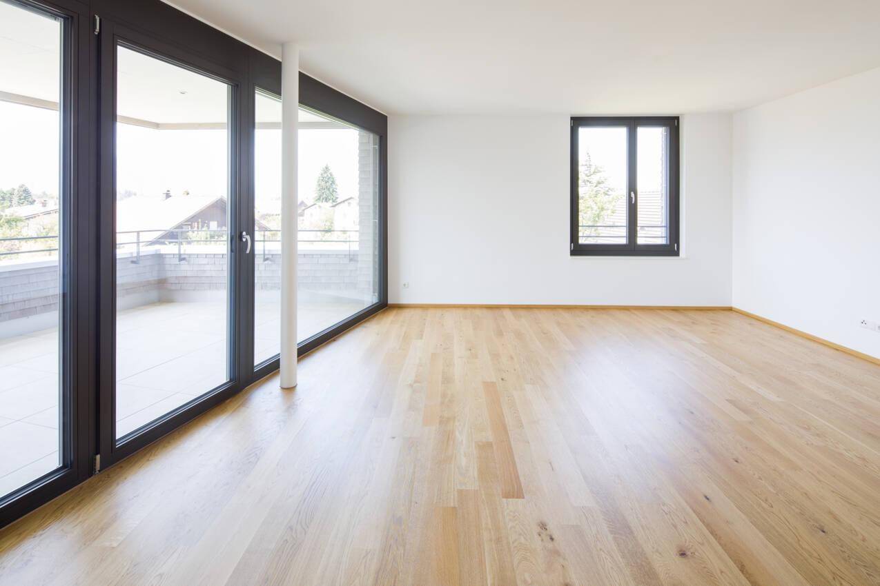 Heller Wohnraum mit großen Fenstern, Holzboden und Zugang zu einem Balkon oder einer Terrasse.