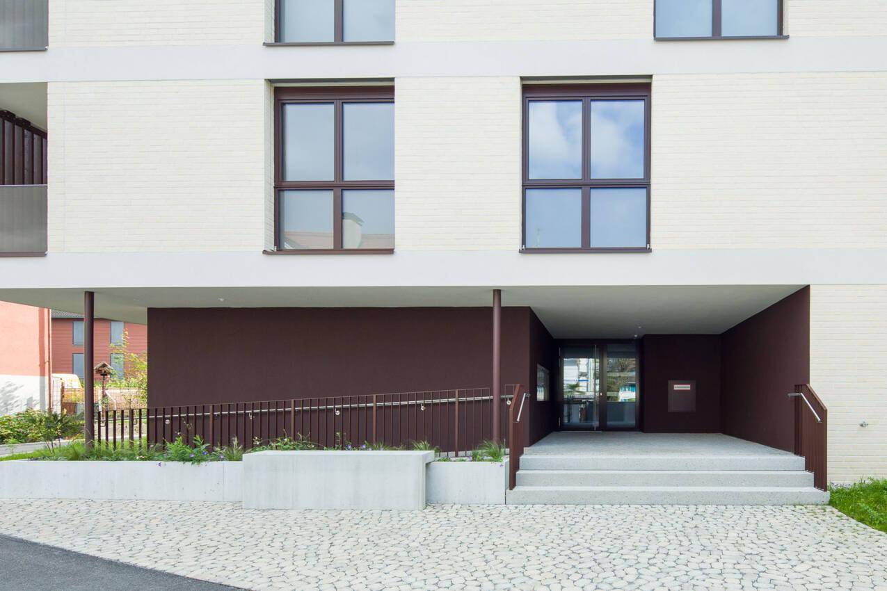Moderner Gebäudeeingang mit Rampe und Treppe, barrierefrei gestaltet.