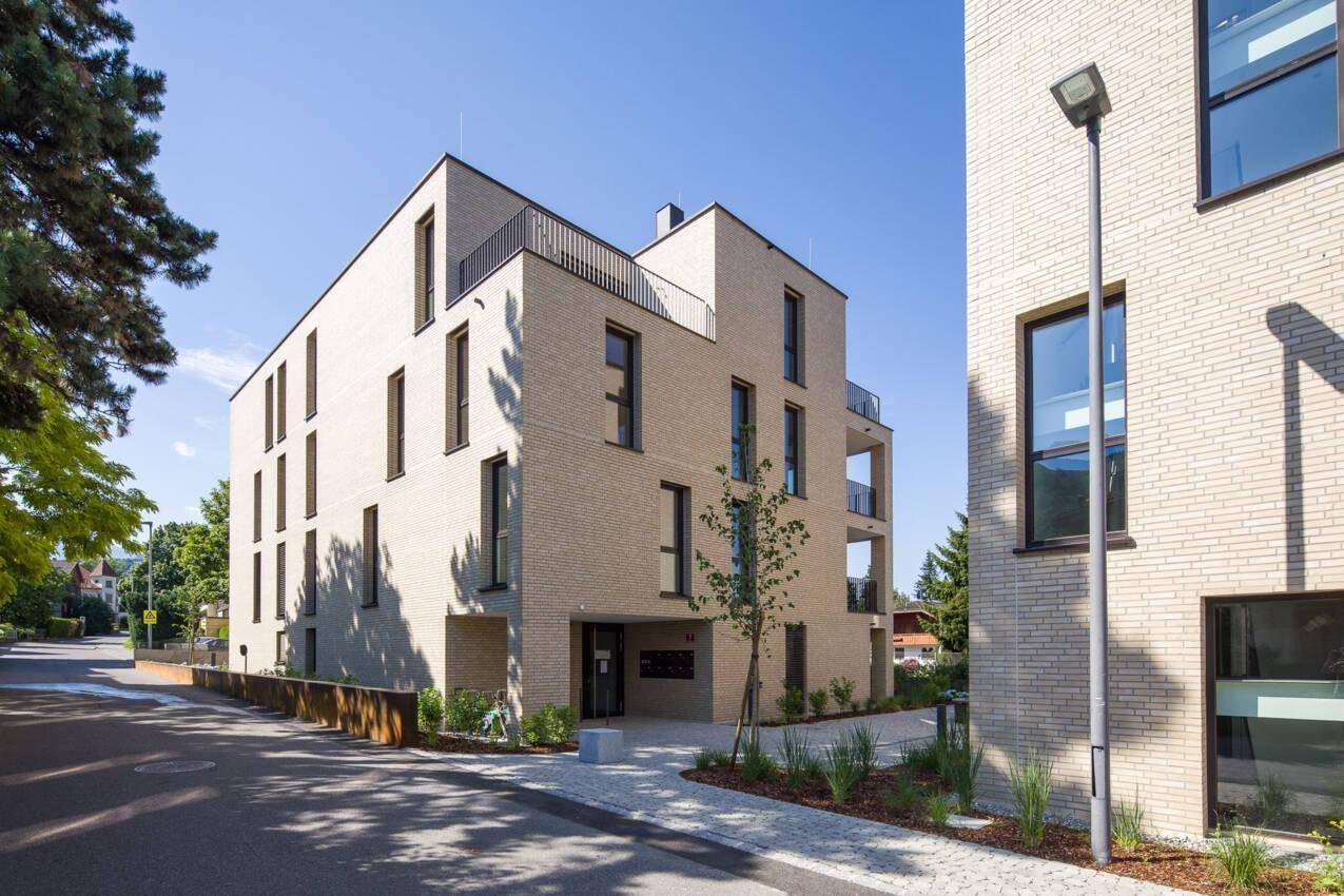 Moderne Wohngebäude mit heller Ziegelfassade und großen Fenstern an einer Straße.