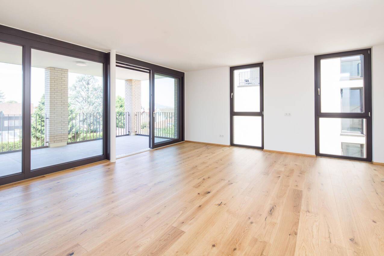 Geräumiger Wohnbereich mit Echtholzboden und großen Schiebetüren zum Balkon.
