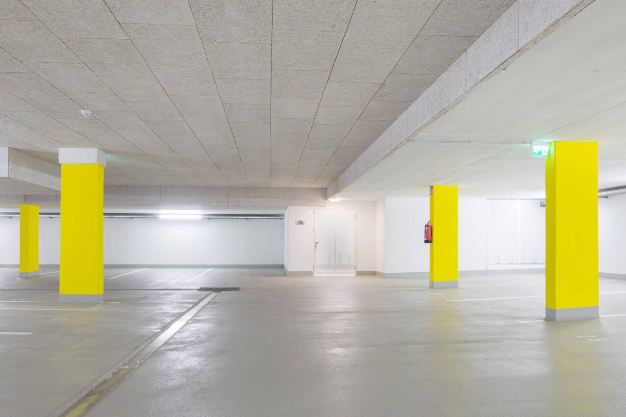 Geräumige Tiefgarage mit hellen Wänden und gelben Säulen, bietet ausreichend Parkplätze.