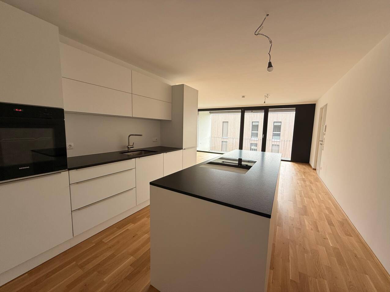 Moderne Einbauküche mit weißen Fronten, dunkler Arbeitsplatte und Kochinsel in offenem Wohnbereich.