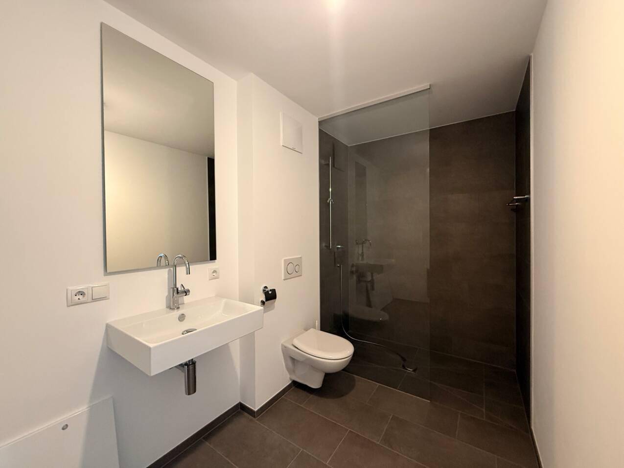 Modernes Badezimmer mit großem Spiegel, wandhängendem WC und ebenerdiger Dusche.