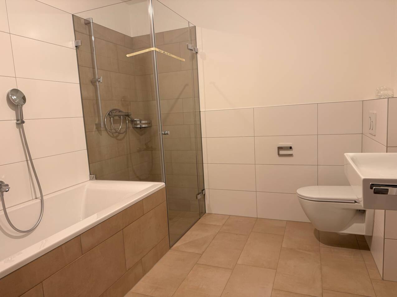 Modernes Badezimmer mit Badewanne, Duschkabine und hellen Fliesen an Wänden und Boden.