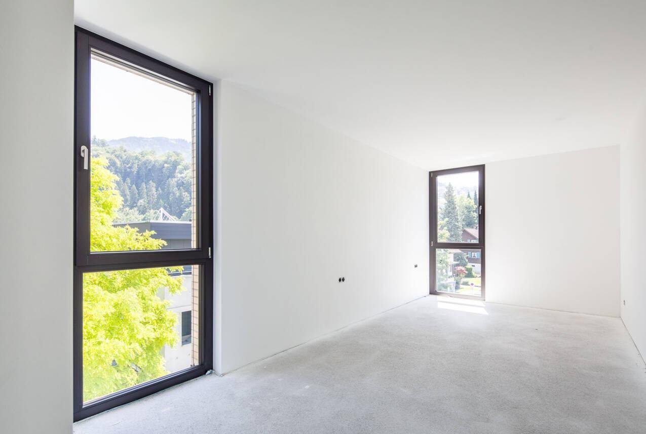 Heller, unfertiger Raum mit großen Fenstern und Blick ins Grüne, ideal als Schlafzimmer.