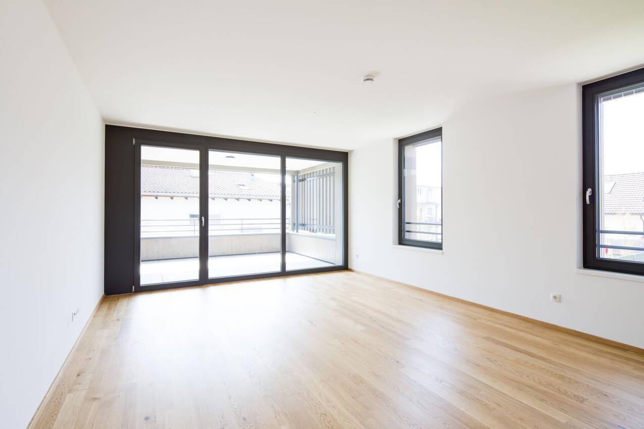 Geräumiges, helles Wohnzimmer mit hellem Holzboden und großem Zugang zum Balkon, bereit zur Einrichtung.
