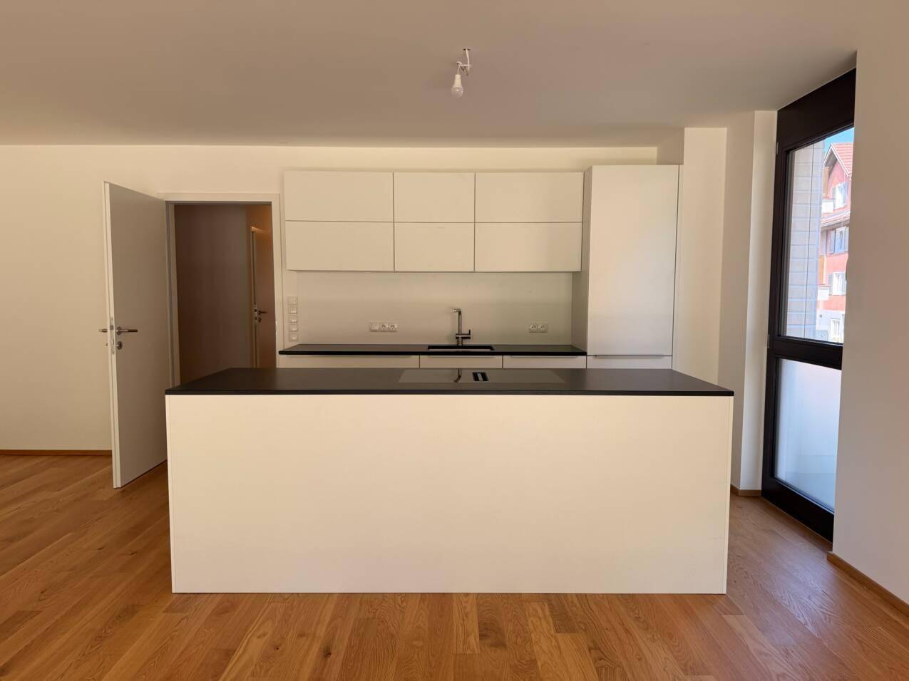 Moderne, helle Küche mit Kochinsel, weißen Schränken, dunkler Arbeitsplatte und Holzboden.