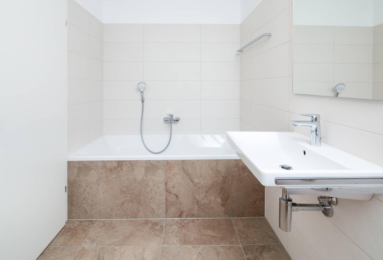 Helles Badezimmer mit Badewanne, modernem Waschbecken und beigefarbenen Fliesen.