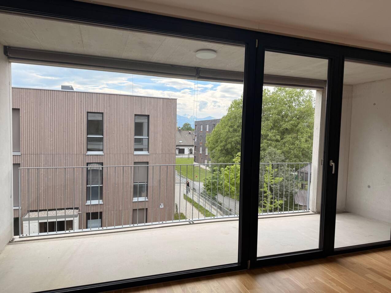 Geräumiger Balkon mit Blick auf die moderne Nachbarbebauung und grüne Bäume.