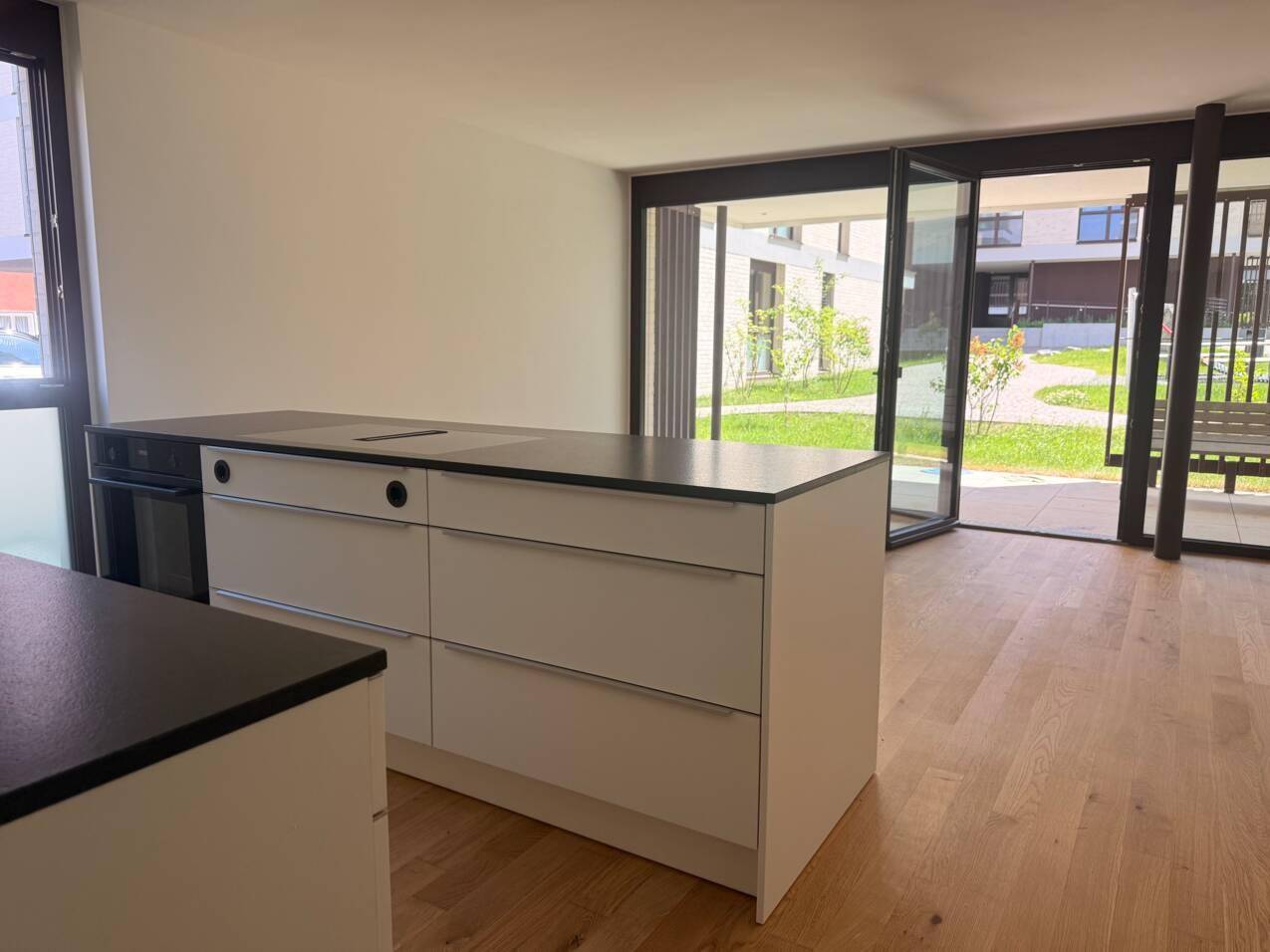Moderne Küche mit Kochinsel und Blick auf die Terrasse sowie den grünen Gemeinschaftsgarten.