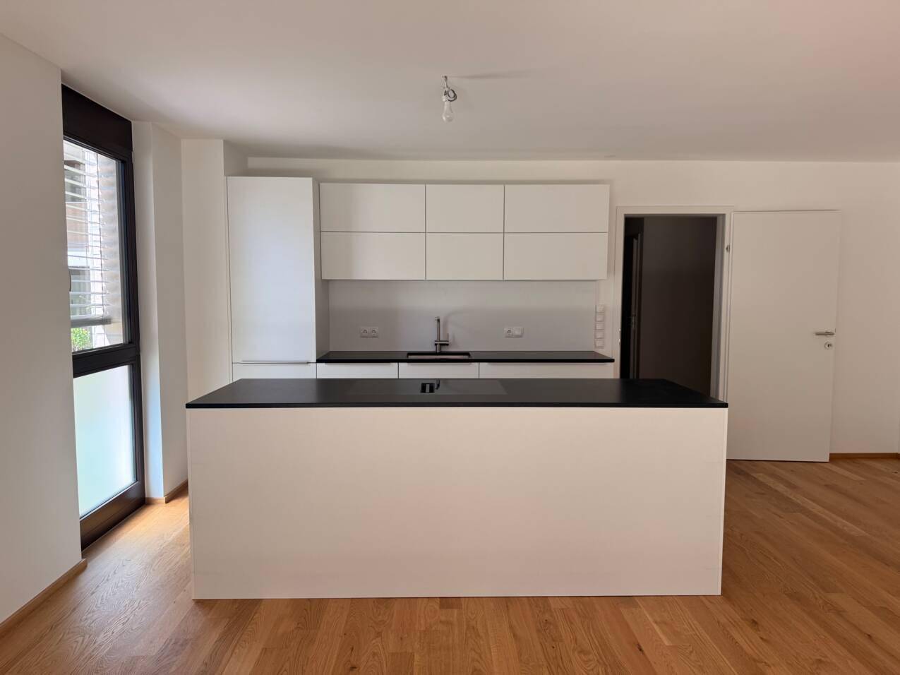 Moderne Einbauküche mit weißen Schränken, dunklen Arbeitsplatten und einer Kücheninsel.