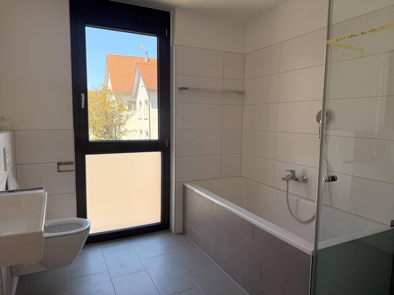 Helles Badezimmer mit Badewanne, Dusche, WC und Fenster, ausgestattet mit modernen Fliesen.