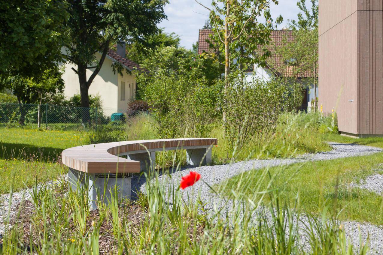 Gepflegte Gartenanlage mit geschwungener Holzbank und Kieswegen für Entspannung im Freien.