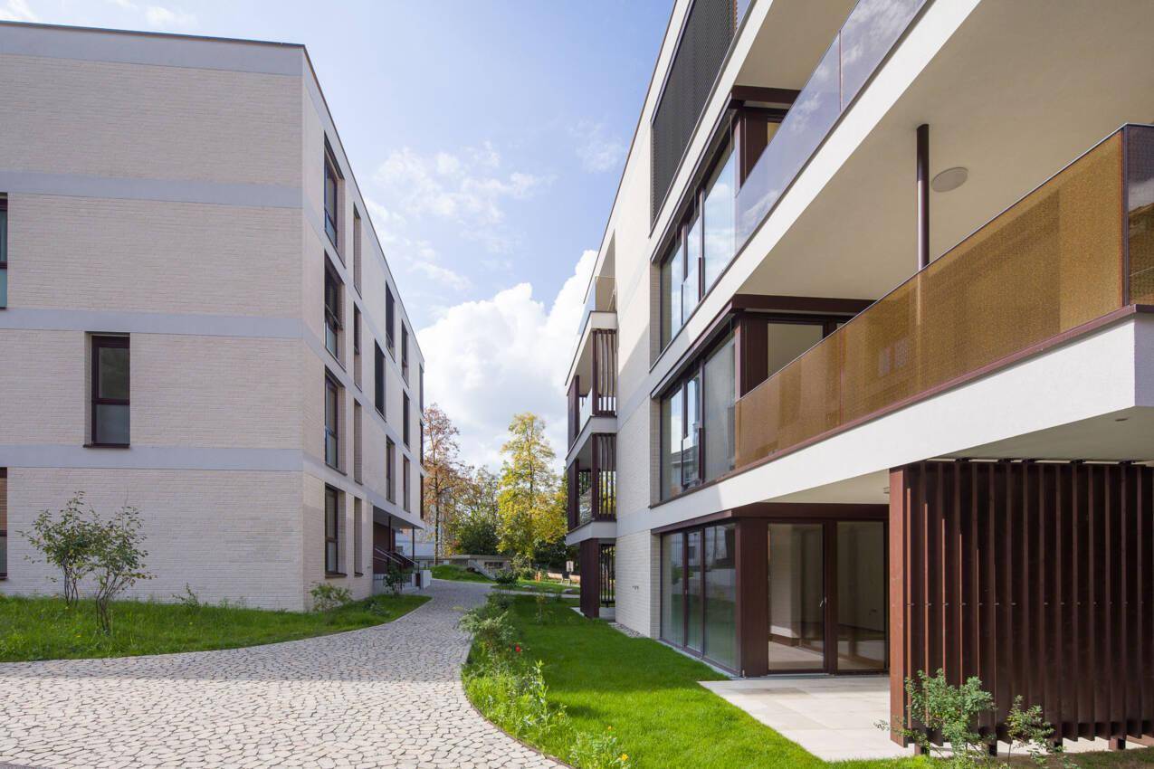 Gepflasterter Weg zwischen zwei modernen Wohngebäuden mit Grünflächen und Bäumen.