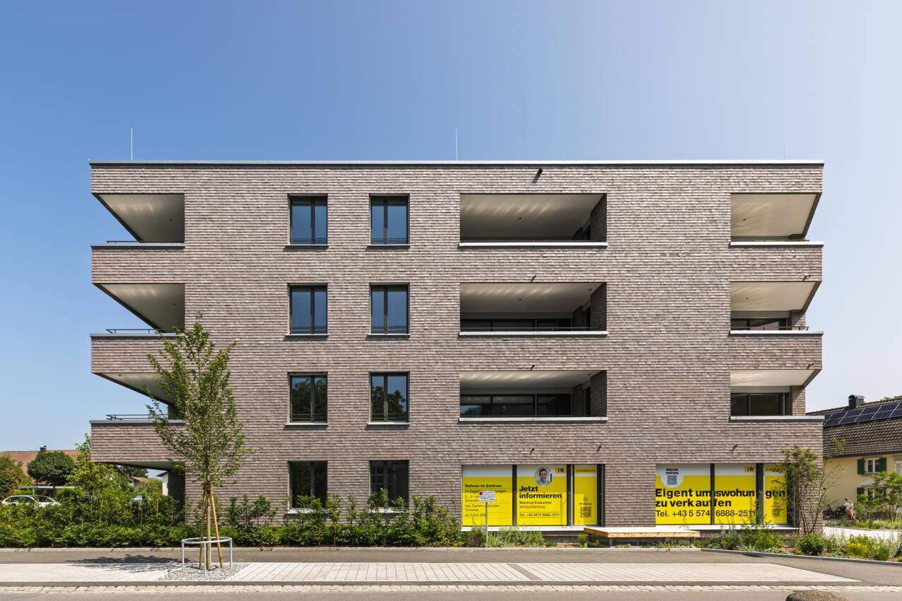 Ansicht der modernen Wohnanlage mit mehreren Balkonen und Holzschindelfassade unter blauem Himmel.