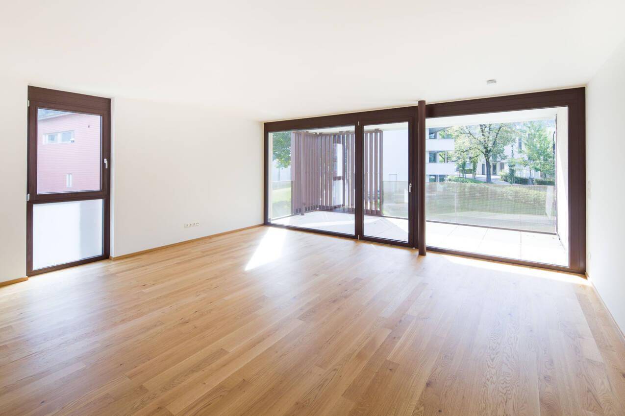 Helles Wohnzimmer mit Eichenparkett, großen Fenstern und Zugang zu einem Balkon.