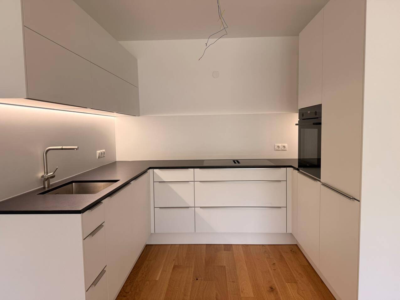 Moderne Küche mit weißen Schränken, dunkler Arbeitsplatte, Einbauofen und Holzfußboden unter Dachschräge.