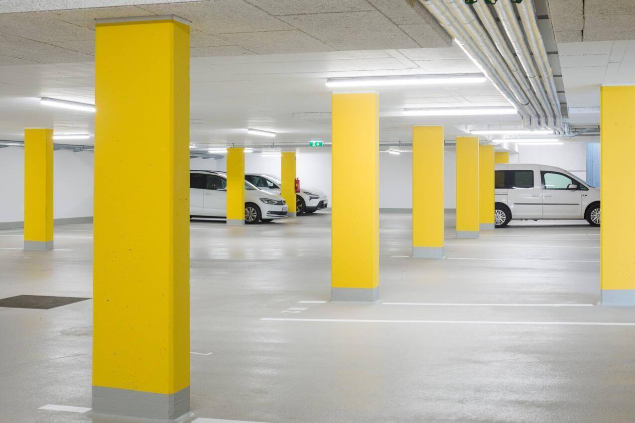Tiefgarage mit leuchtend gelben Säulen und ausreichend Stellplätzen für Fahrzeuge.