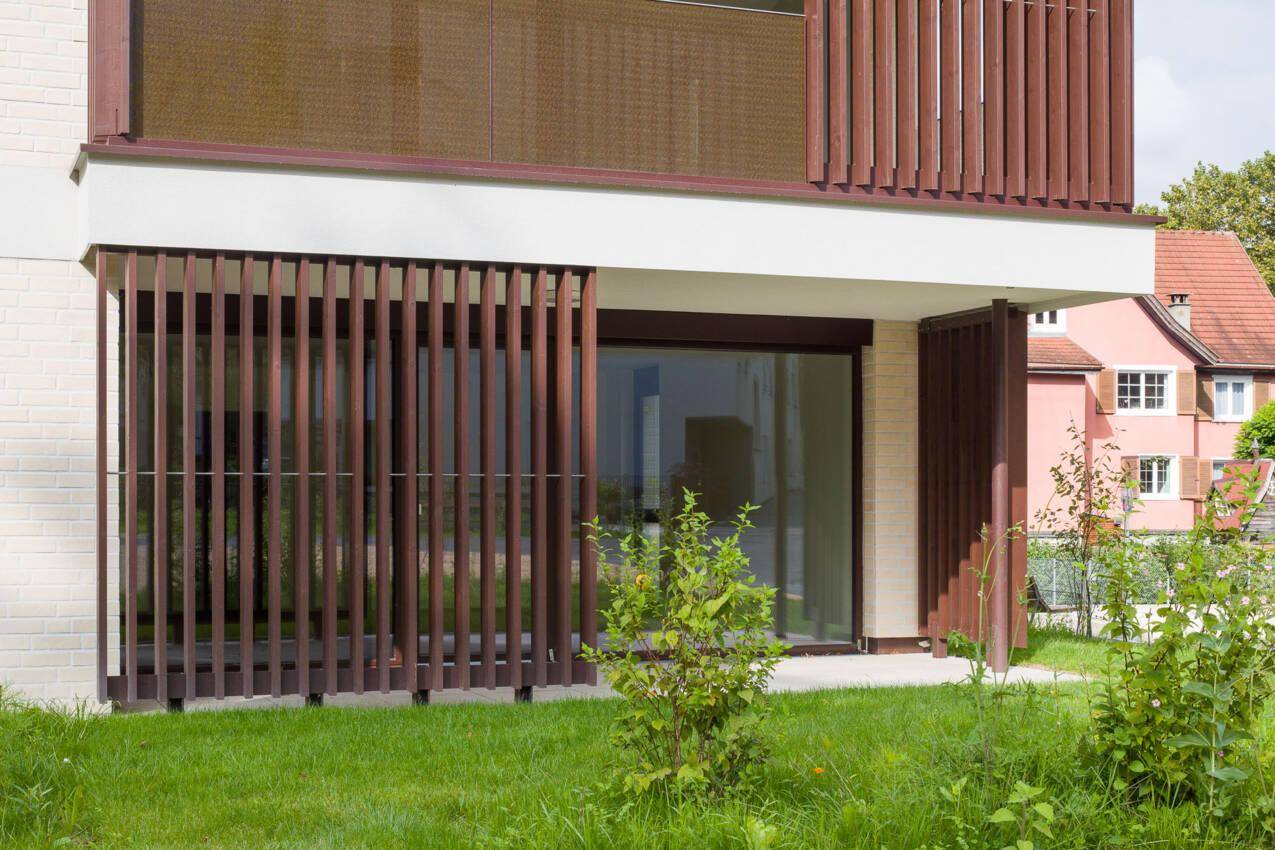 Erdgeschossfassade eines modernen Gebäudes mit großen Fenstern und dekorativen Holzlamellen.