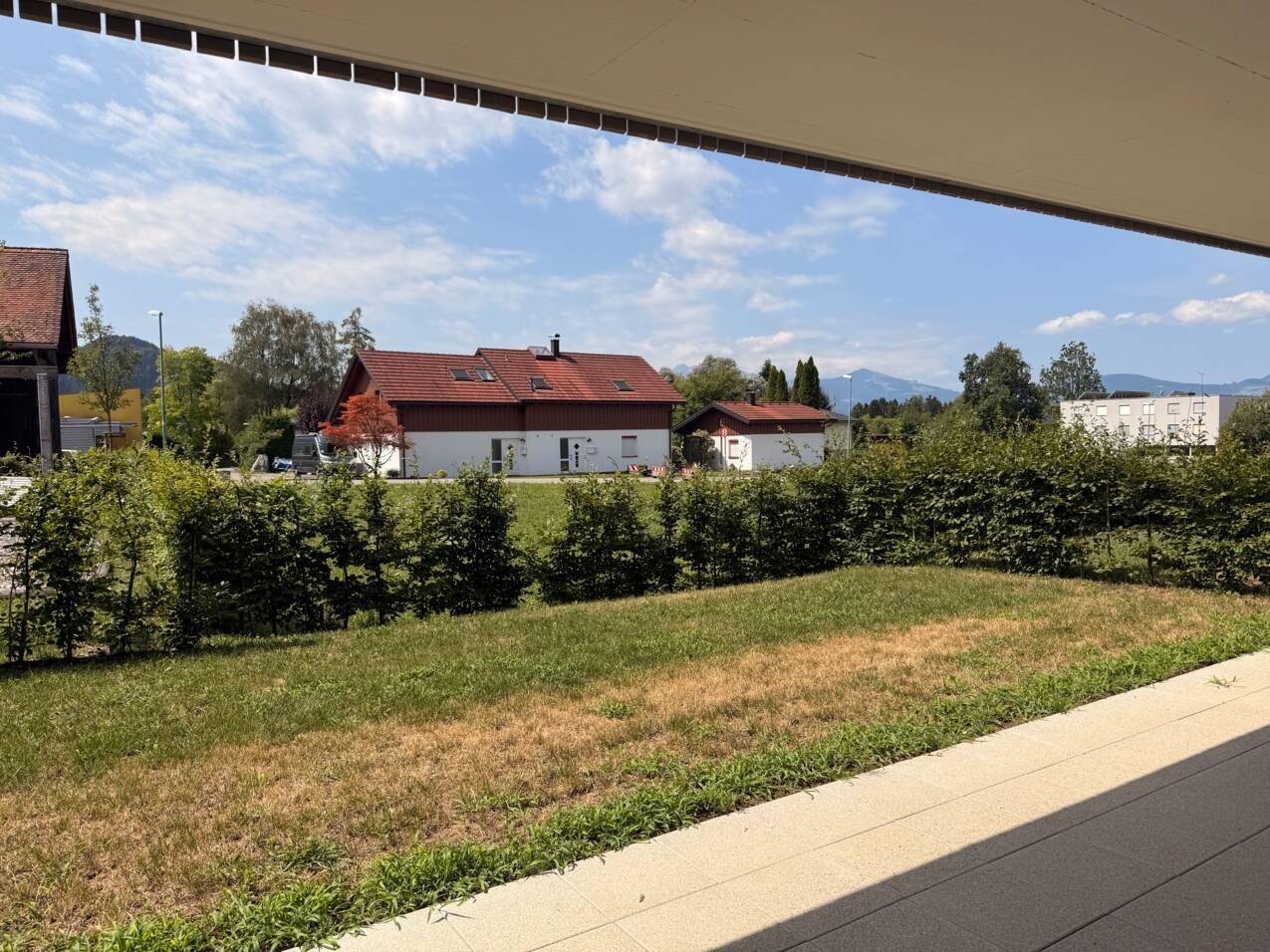 Blick von der Terrasse auf den grünen Garten und die umliegende Wohngegend mit Häusern.
