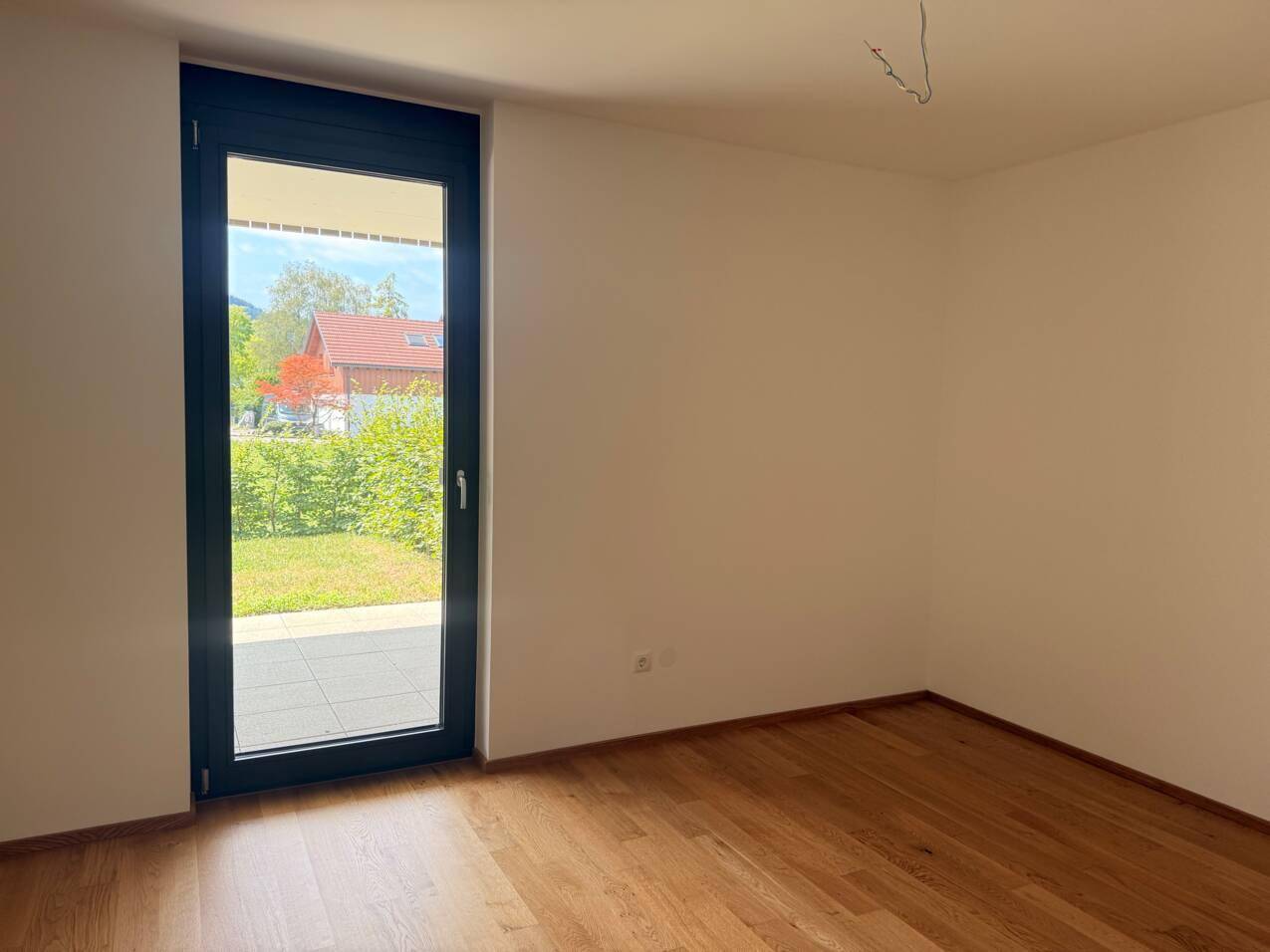 Helles, leeres Zimmer mit Holzboden und großem Fenster mit Zugang zur Terrasse.