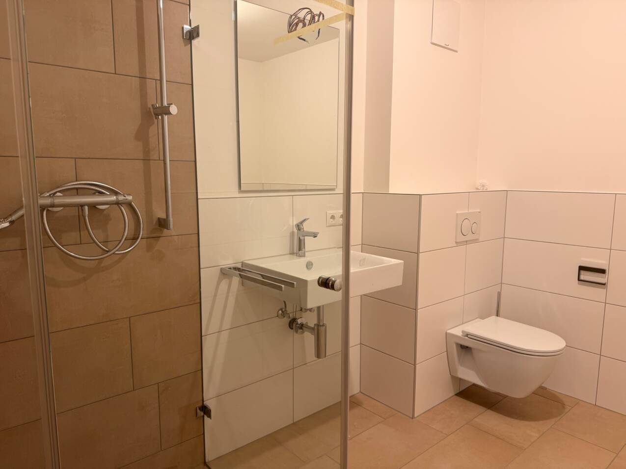 Modernes Badezimmer mit ebenerdiger Dusche, wandhängendem WC und hellen Fliesen.